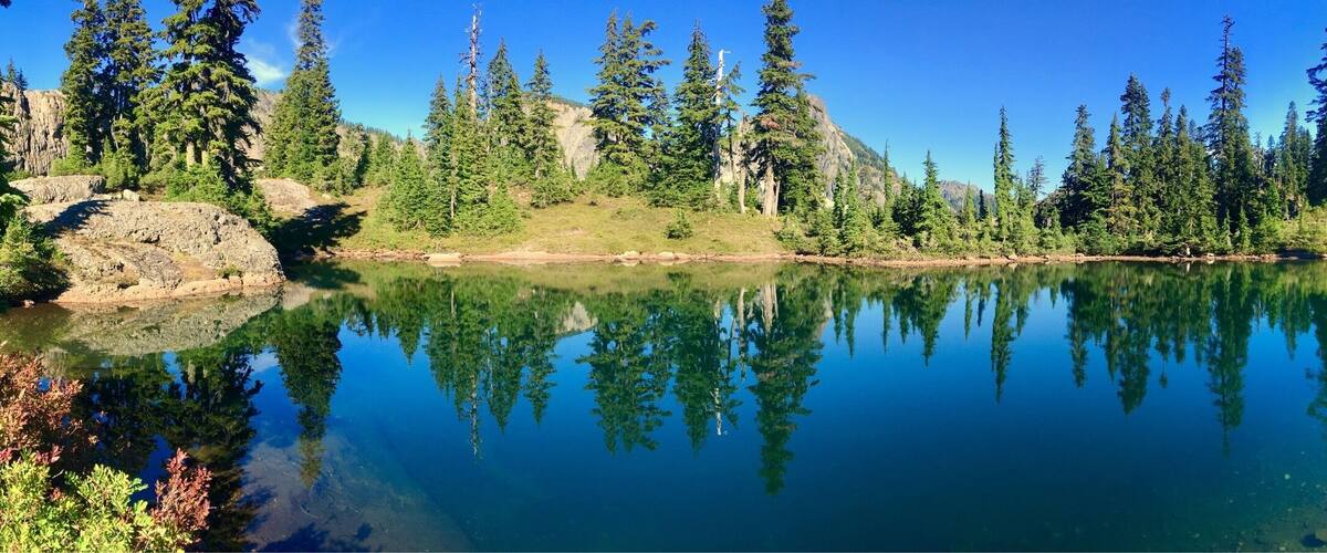 Ein klarer See, umgeben von dichtem Wald und felsigem Gelände.