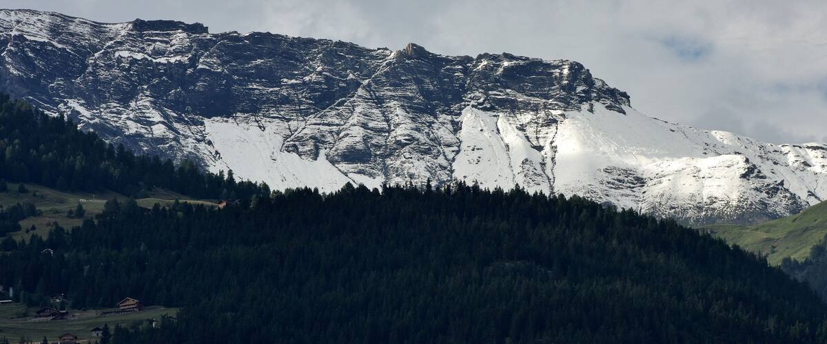 A snow-capped mountain with a forested valley and a small settlement at its base.
