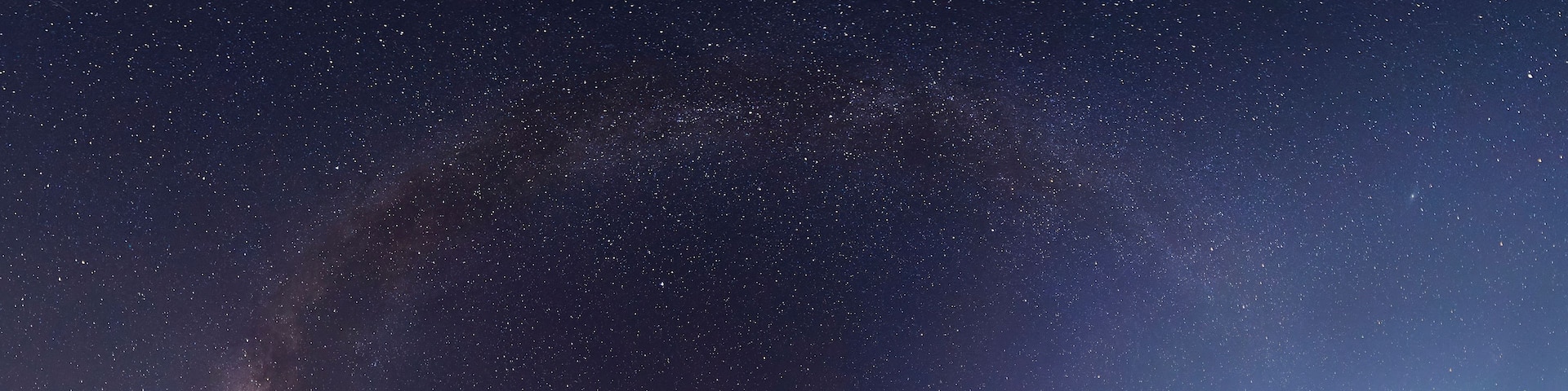 A starry night sky with a visible Milky Way galaxy and a crescent moon.