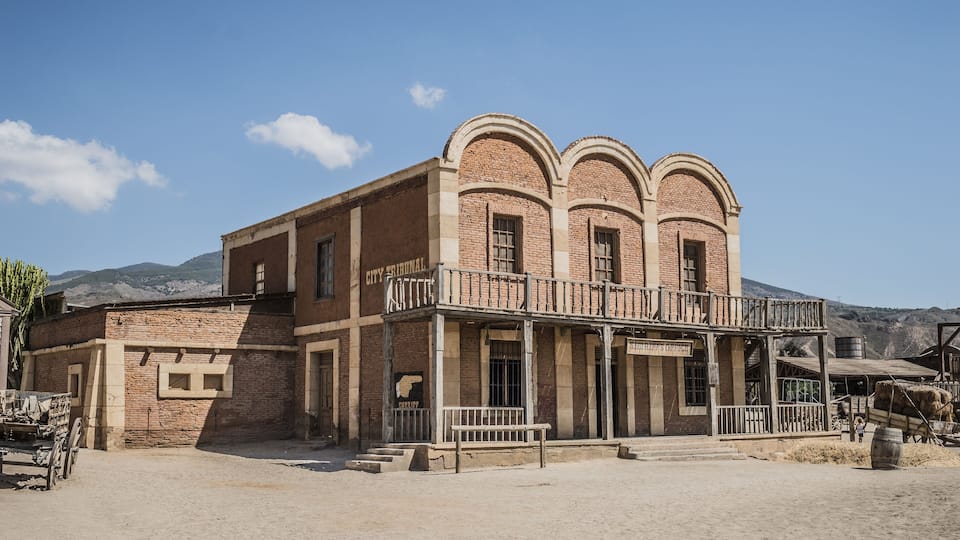 A historic building with arched windows and a balcony, surrounded by a desert landscape.