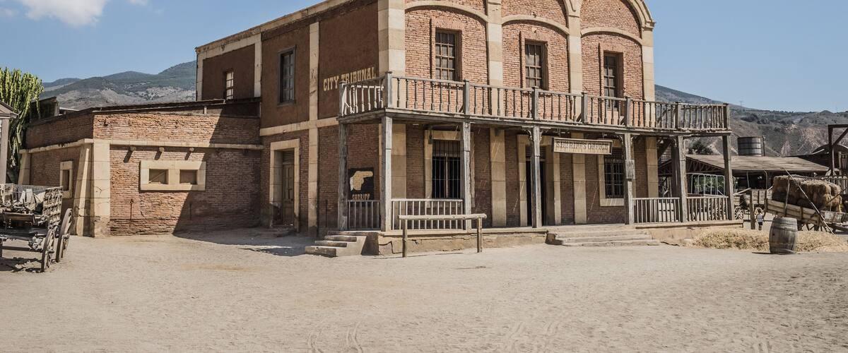 A historic building with arched windows and a balcony, surrounded by a desert landscape.
