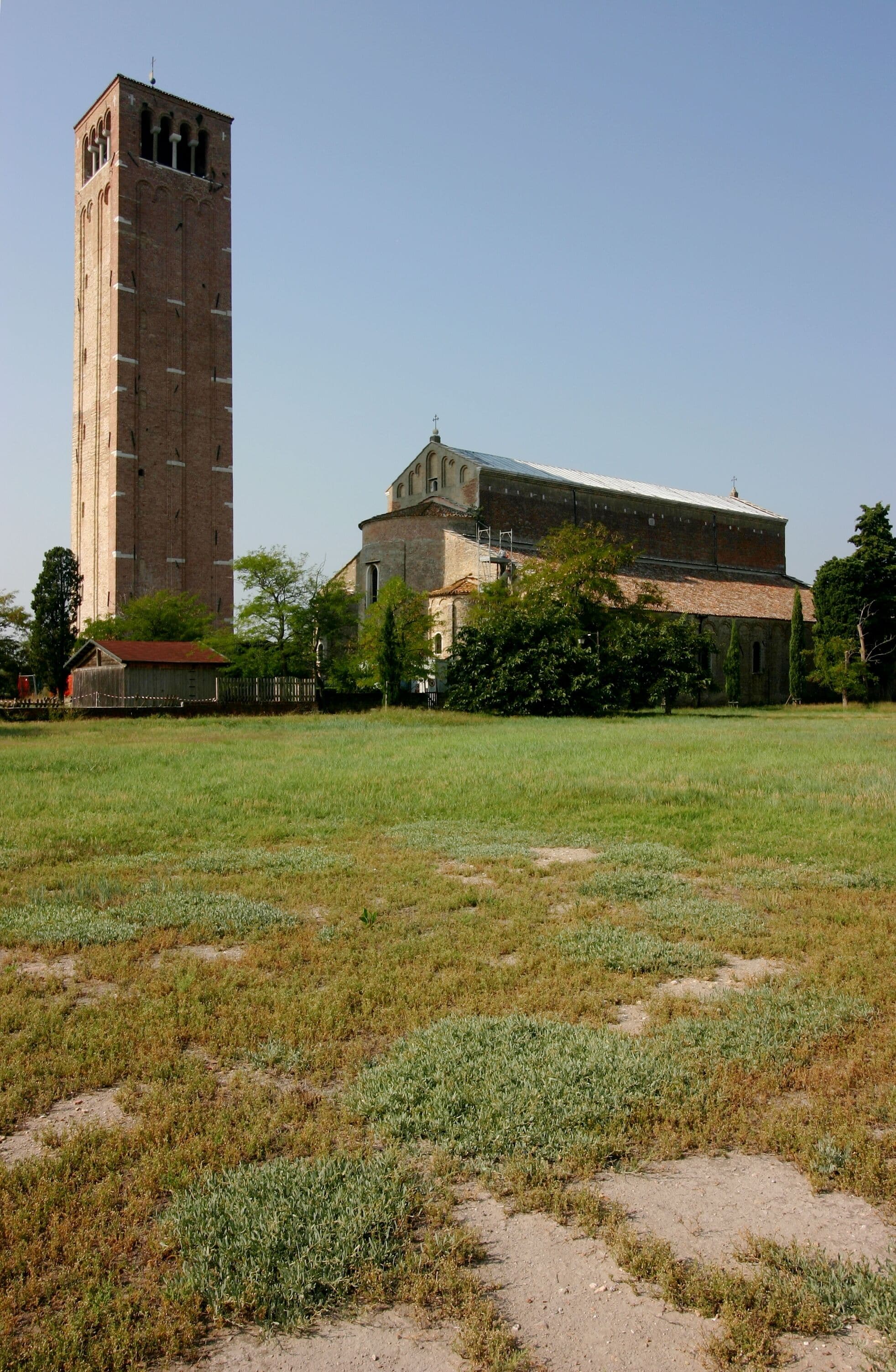 A tall brick tower and a large building with a tiled roof, surrounded by a grassy field and trees.