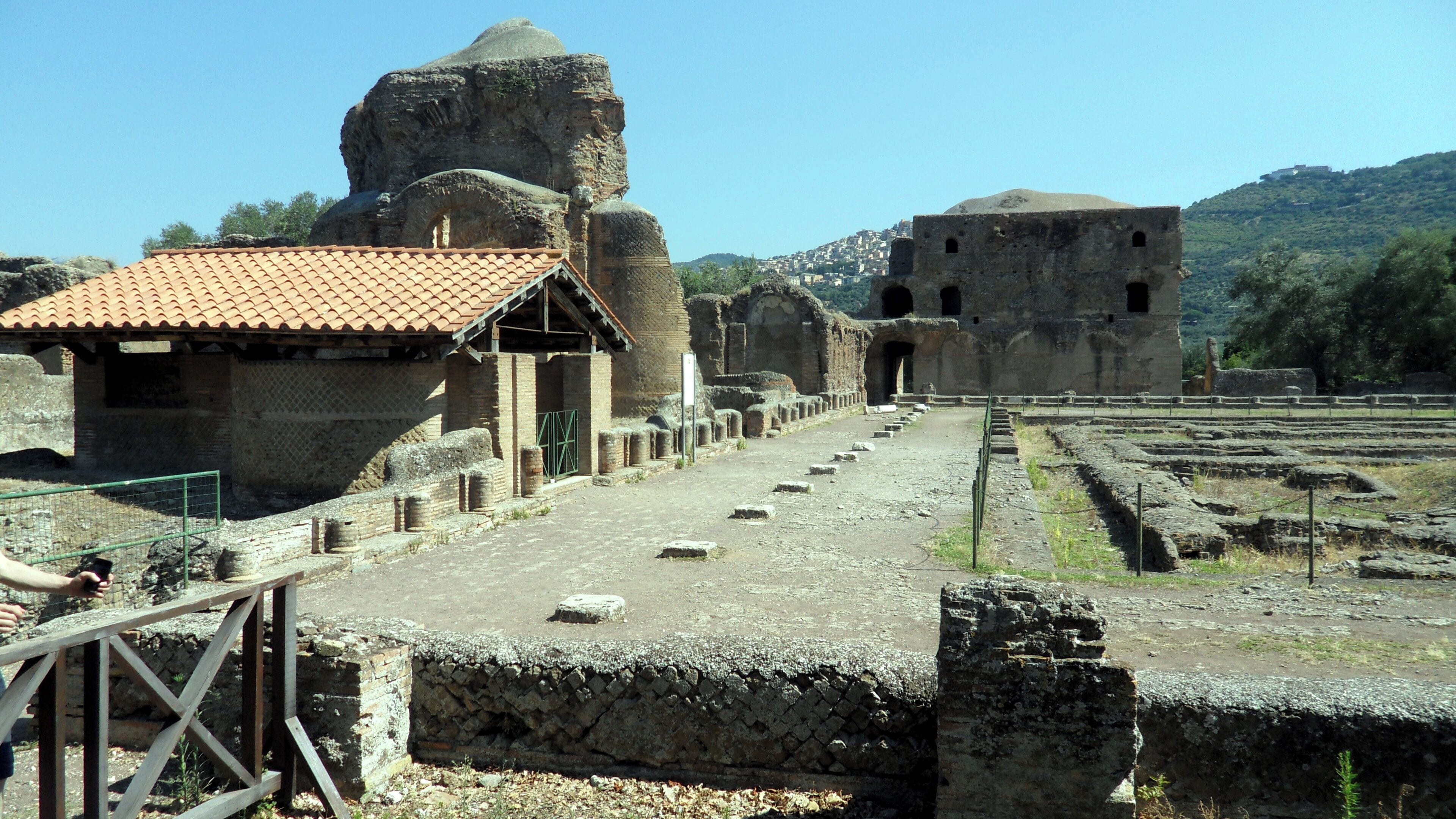 Ancient ruins with a stone pathway, a small building with a tiled roof, and a large rock formation.