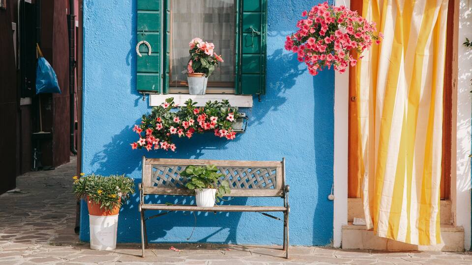 A blue building with a wooden bench, potted plants, and hanging flowers.