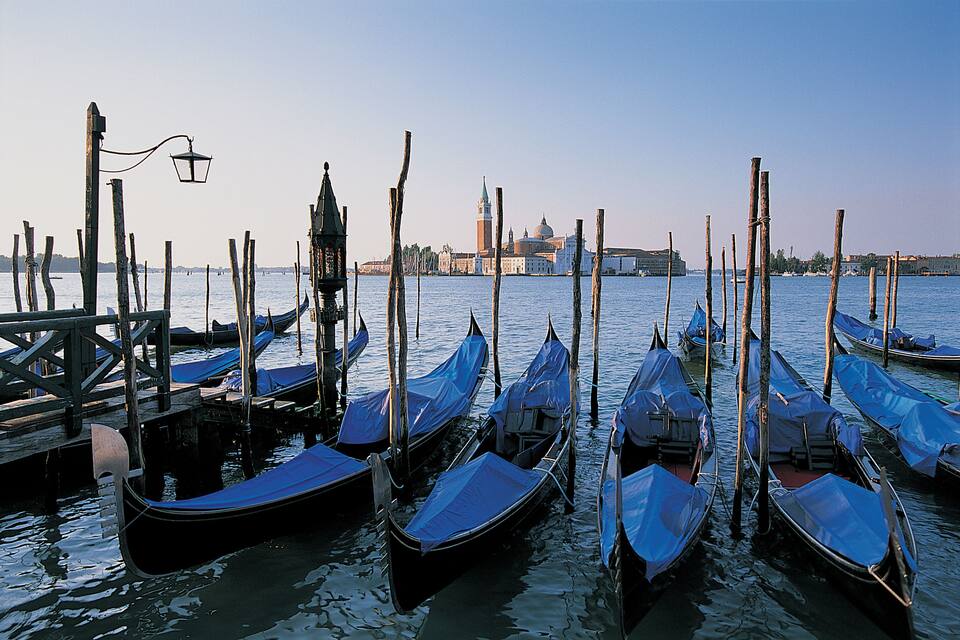 A row of gondolas docked at a pier with a historic building in the background.