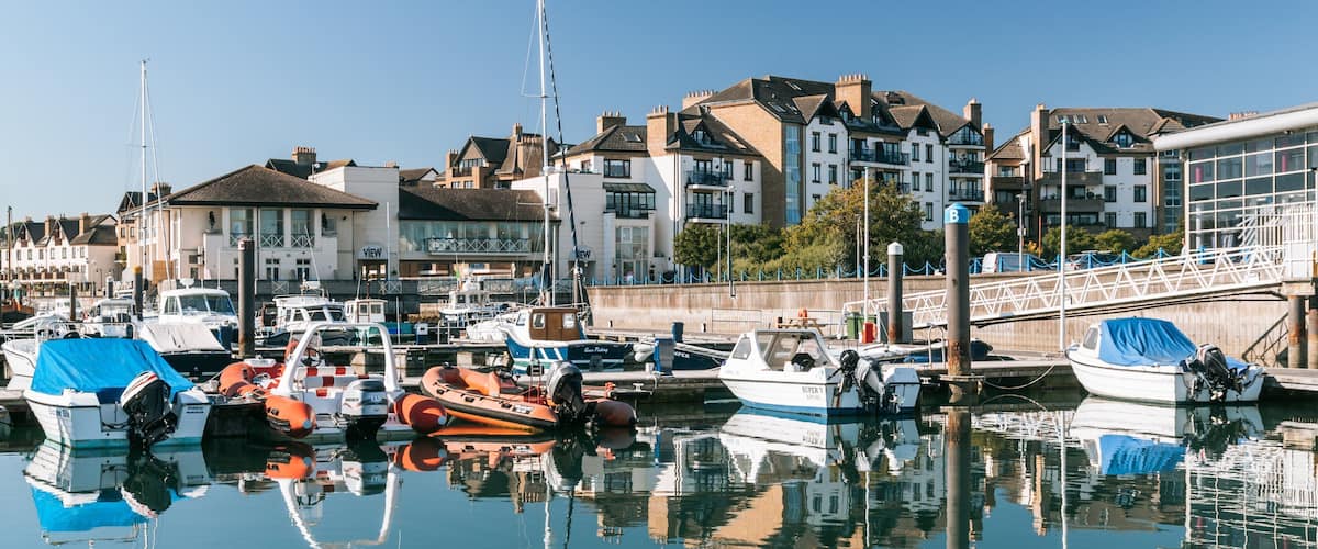 A marina with various boats docked, surrounded by residential buildings and a clear blue sky.