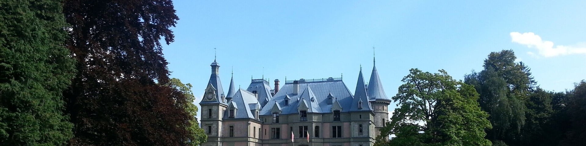 A large, historic building with multiple towers and a well-maintained lawn in front.