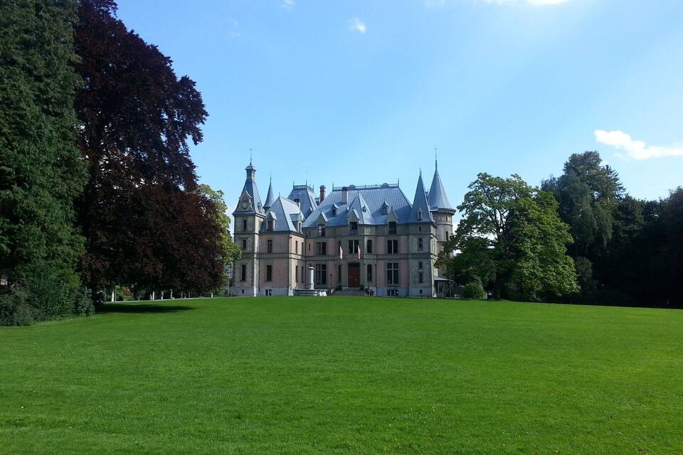 A large, historic building with multiple towers and a well-maintained lawn in front.