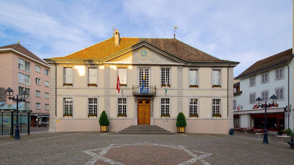 A historic building with a clock tower, a central entrance with steps, and flags on the roof.