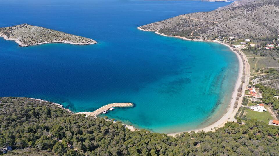A coastal landscape with clear turquoise waters, a sandy beach, and a forested area.