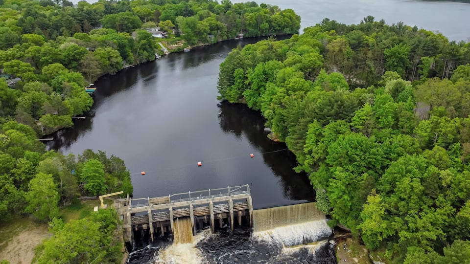 A dam with water flowing over it, surrounded by dense green forest and a large lake.