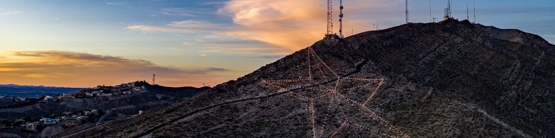 A mountainous landscape with a star-shaped light installation and communication towers.