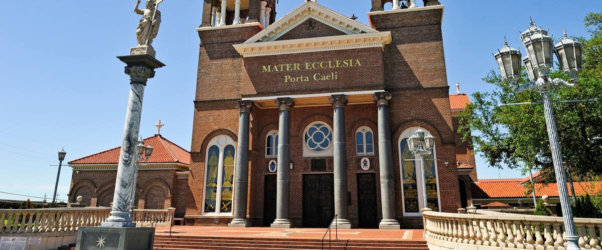 A large brick church with two bell towers and statues on top.