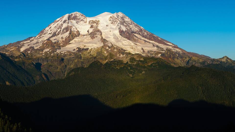 A snow-capped mountain with forested valleys.