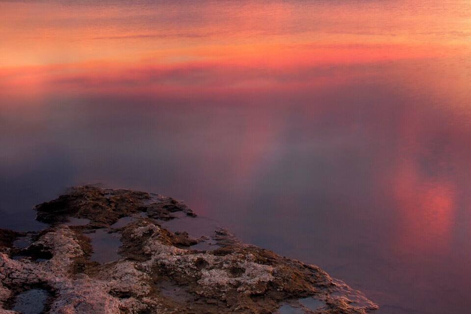 A sunset over a calm lake with rocky shores.