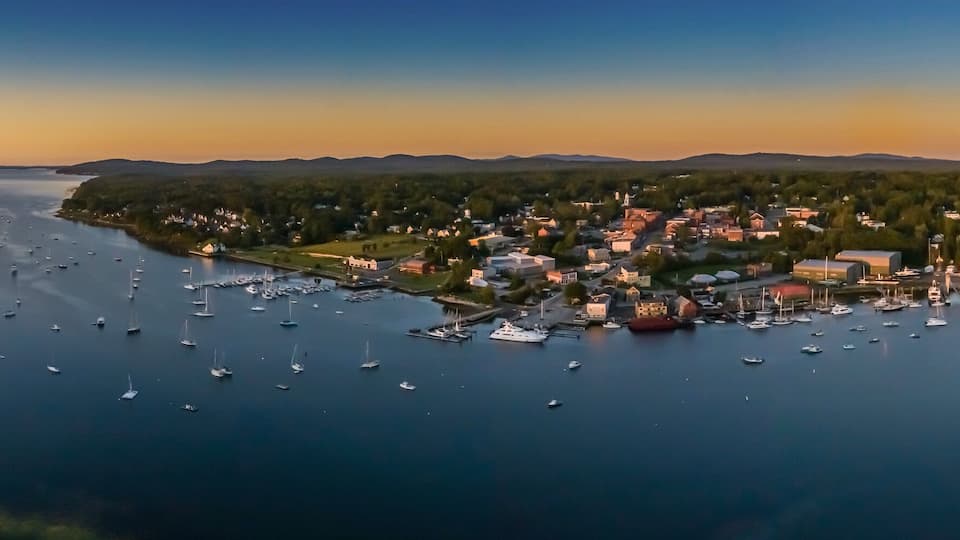 A coastal town with a marina filled with boats, surrounded by forested hills.