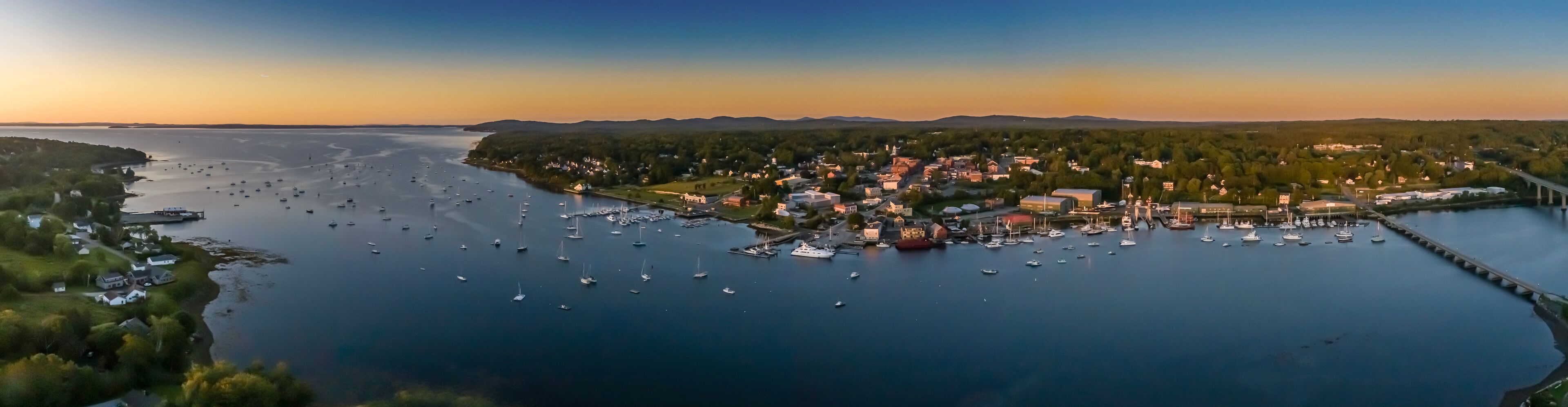 A coastal town with a marina filled with boats, surrounded by forested hills.