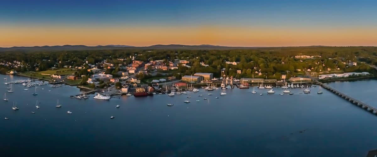 A coastal town with a marina filled with boats, surrounded by forested hills.