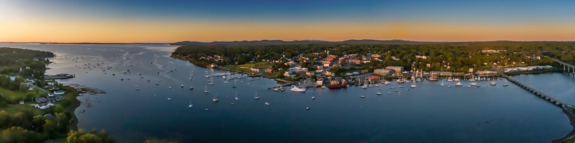 A coastal town with a marina filled with boats, surrounded by forested hills.