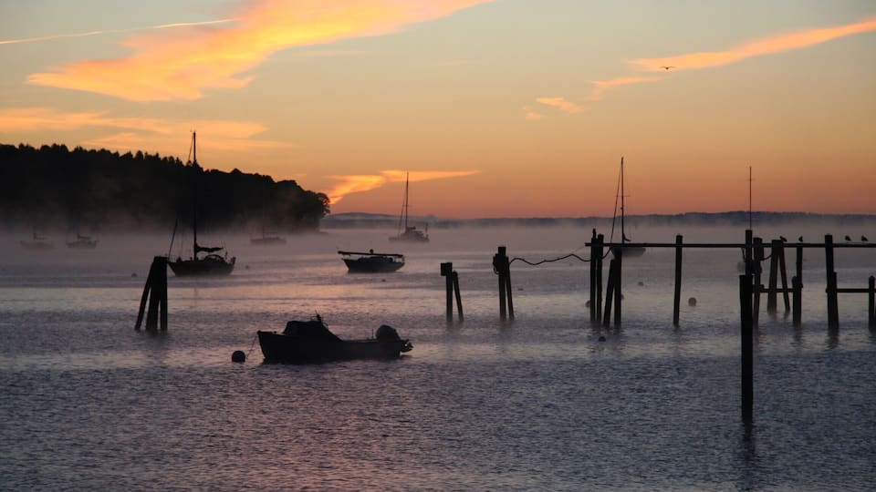 A calm lake at sunset with several boats anchored near wooden docks.
