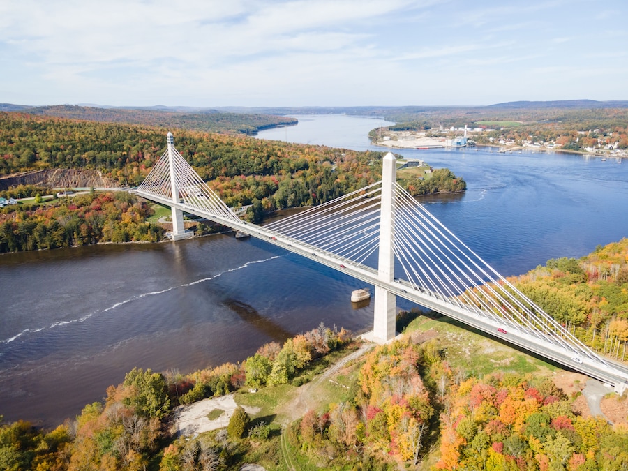 A suspension bridge over a river with autumn foliage and a distant town.
