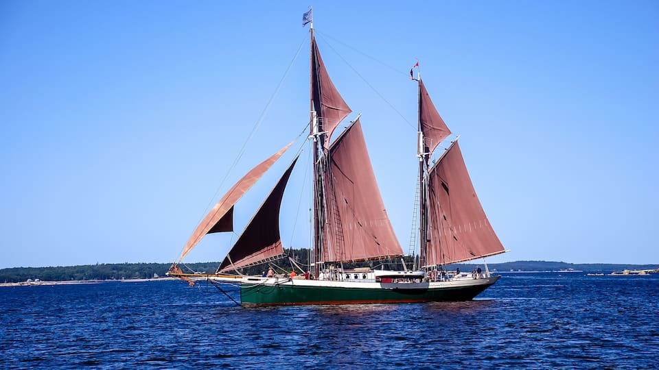 A sailboat with two masts and red sails on a calm sea.