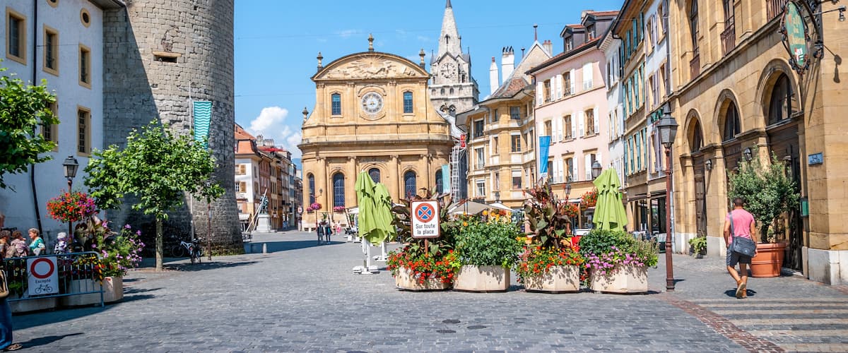 A historic town square with a prominent tower, a church, and colorful flower arrangements.