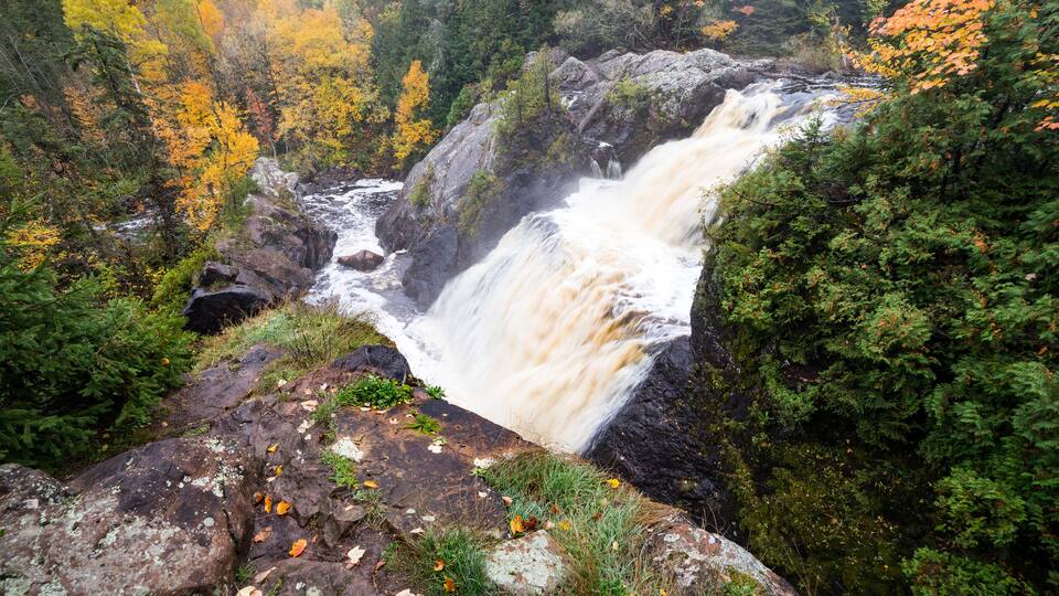 A waterfall cascading over rocks surrounded by autumn-colored trees.