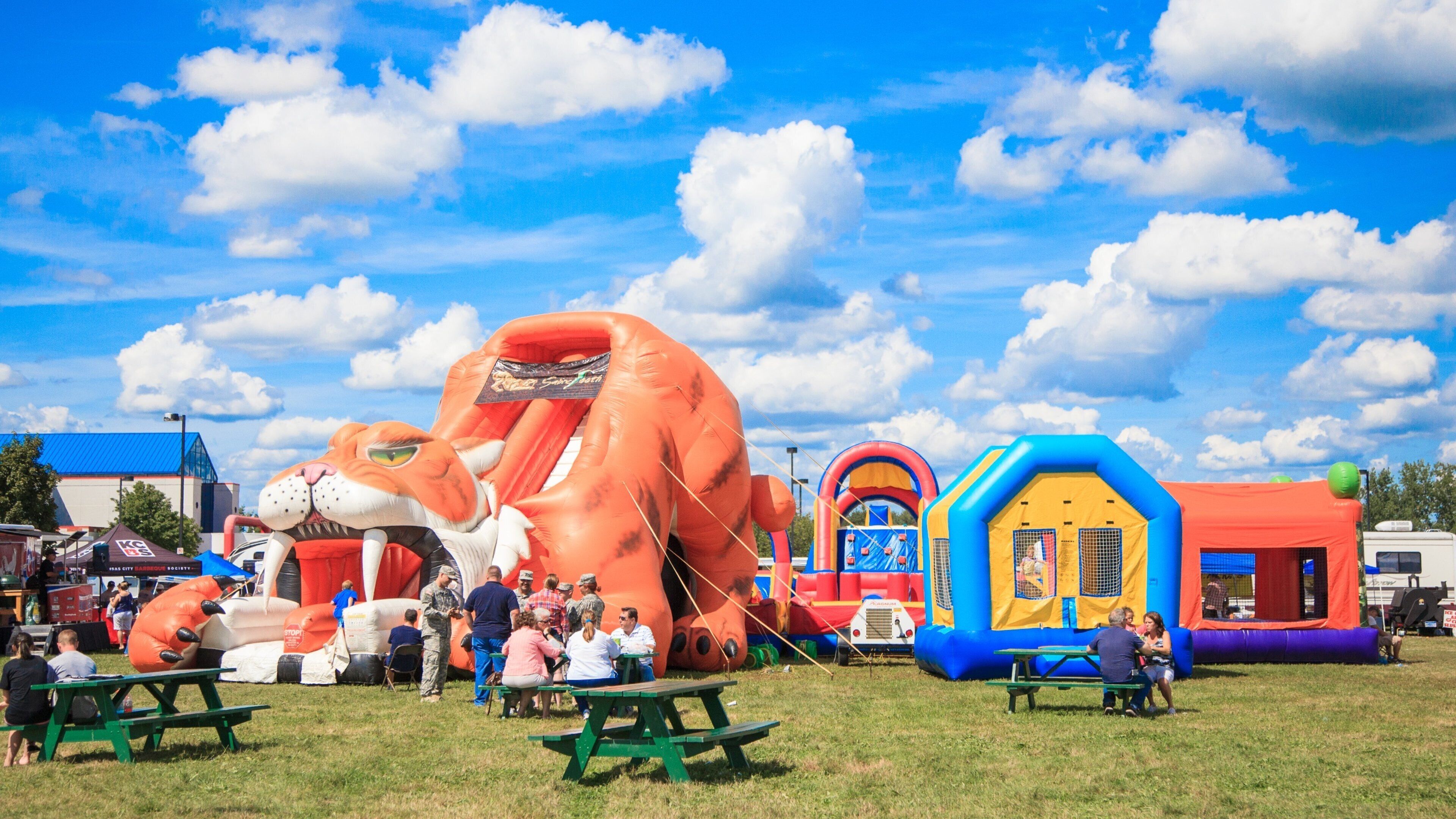 A sunny day at a fair with inflatable rides and picnic tables.