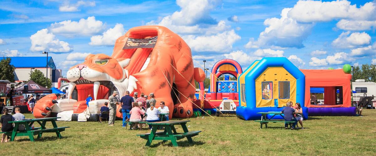 A sunny day at a fair with inflatable rides and picnic tables.