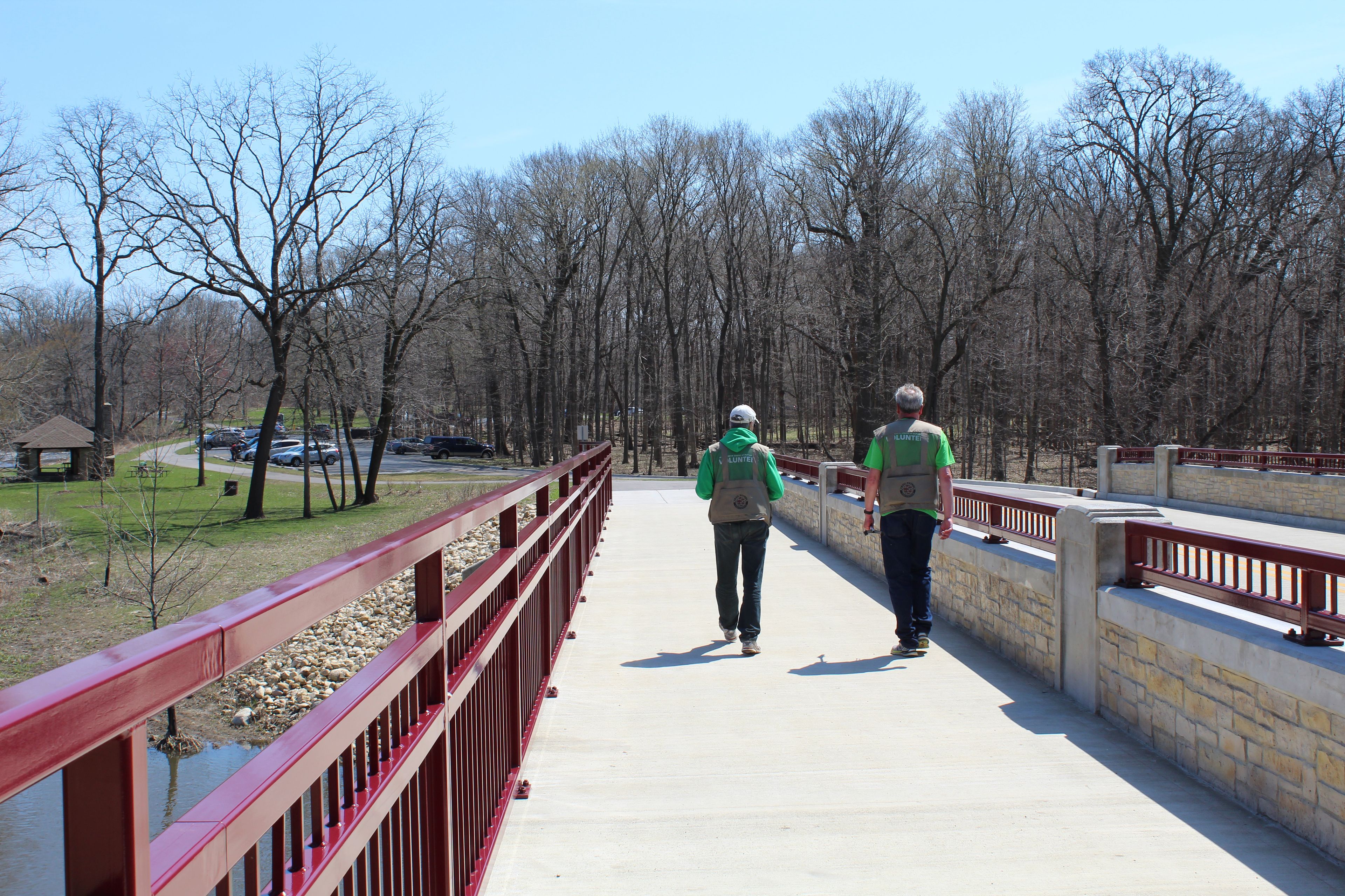 Two elderly male volunteers walking over a bridge over the DuPage River at McDowell Grove Forest Preserve in Naperville, Illinois