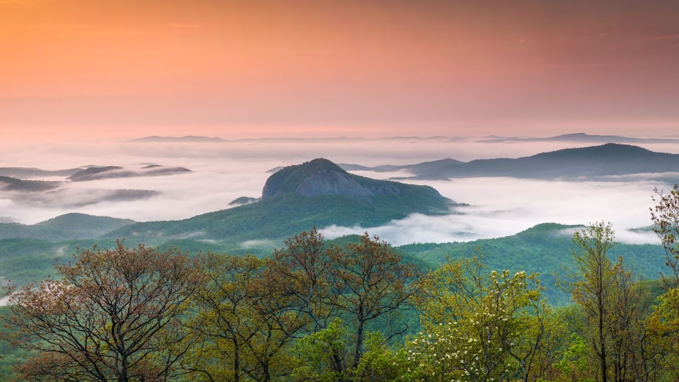 A mountainous landscape with a prominent peak, lush green valleys, and a sunrise or sunset sky.