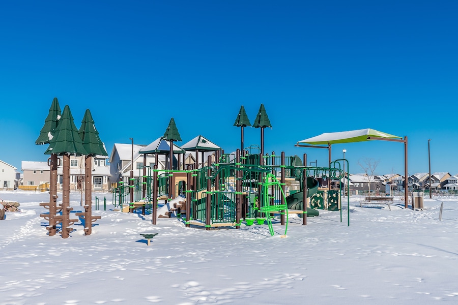 Un parque infantil cubierto de nieve con estructuras de escalada verdes y un paraguas amarillo.