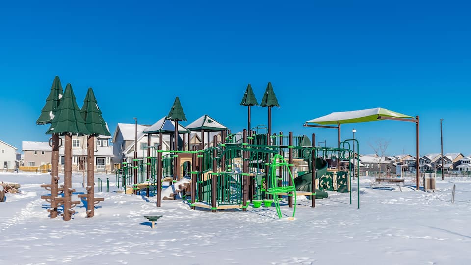 A snow-covered playground with green climbing structures and a yellow umbrella.