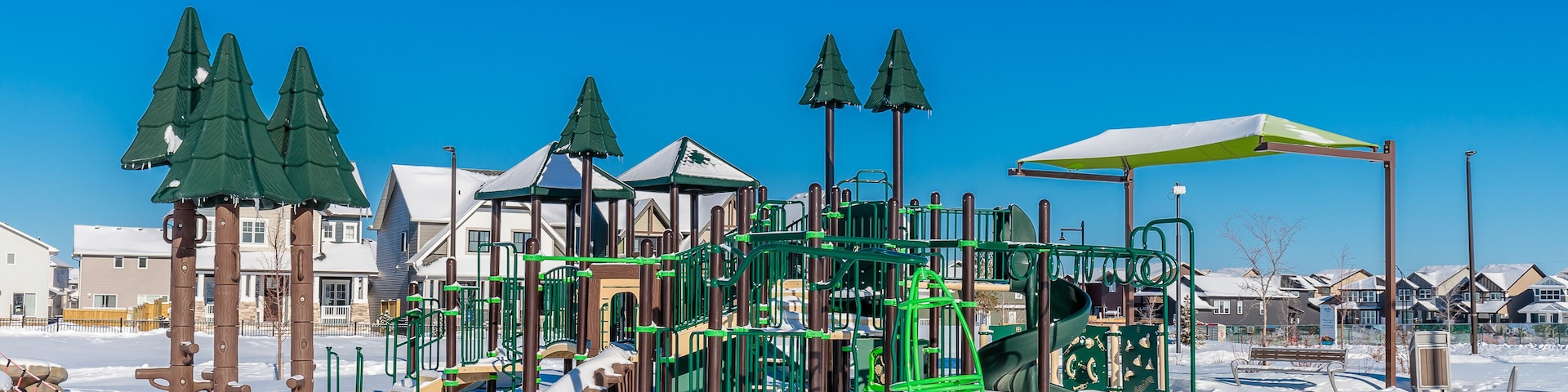 Un parque infantil cubierto de nieve con estructuras de escalada verdes y un paraguas amarillo.