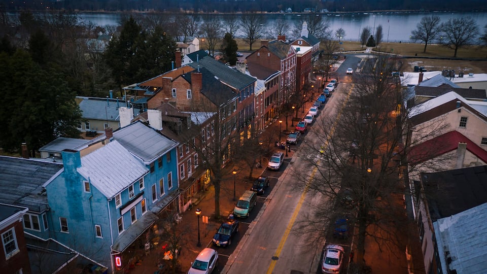 A river with buildings and parked cars along the riverbank.