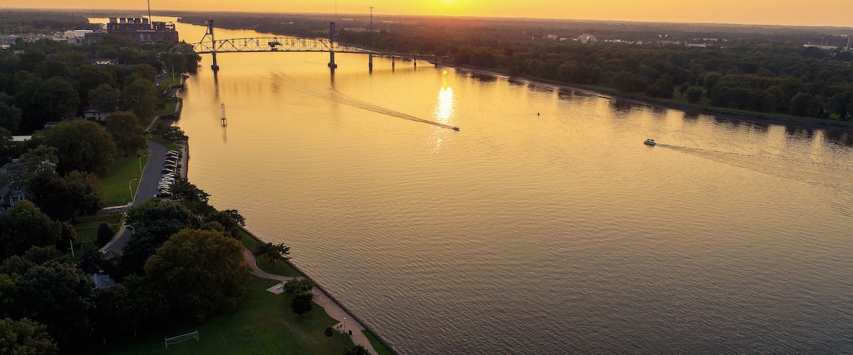 A river with a bridge, a park, and a cityscape in the background.