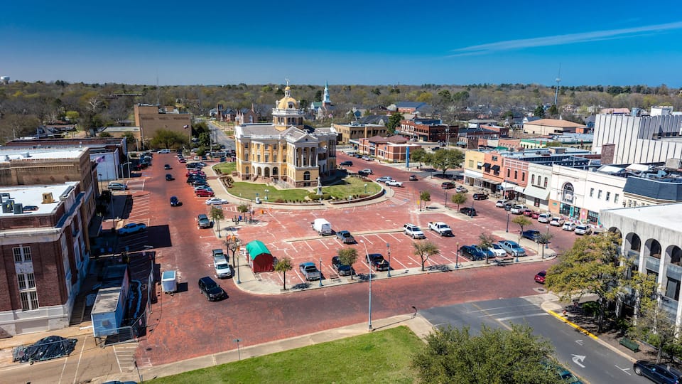 A cityscape with a prominent historic building, a roundabout, and a parking lot.