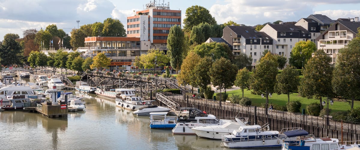A marina with various boats docked, surrounded by residential buildings and trees.