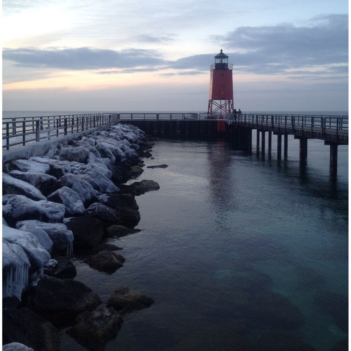 A red lighthouse on a pier with ice-covered rocks.