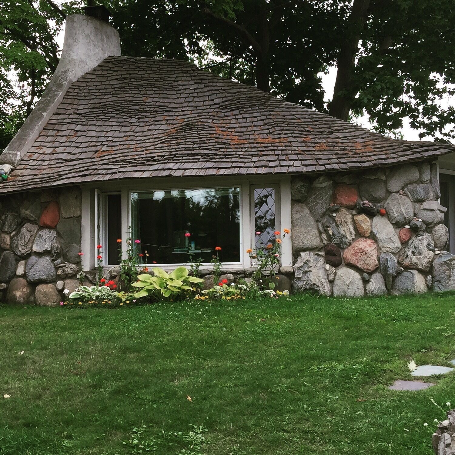 A stone house with a sloped roof and a garden in front.