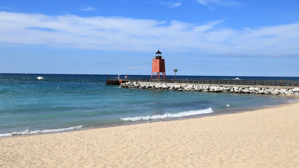 A sandy beach with a red lighthouse and rocky pier extending into the ocean.
