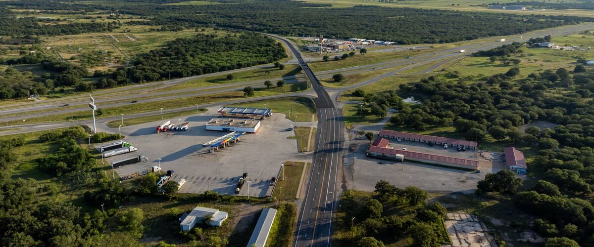 An aerial view of a highway interchange with multiple lanes, surrounded by green fields and sparse buildings.