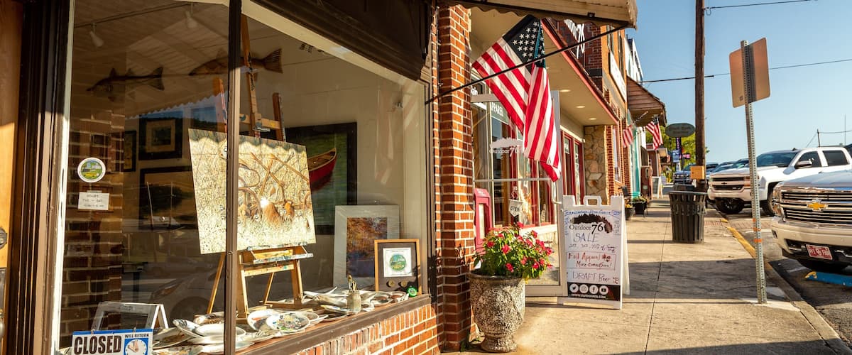 A storefront with American flags, a sign for an outdoor sale, and a closed sign.