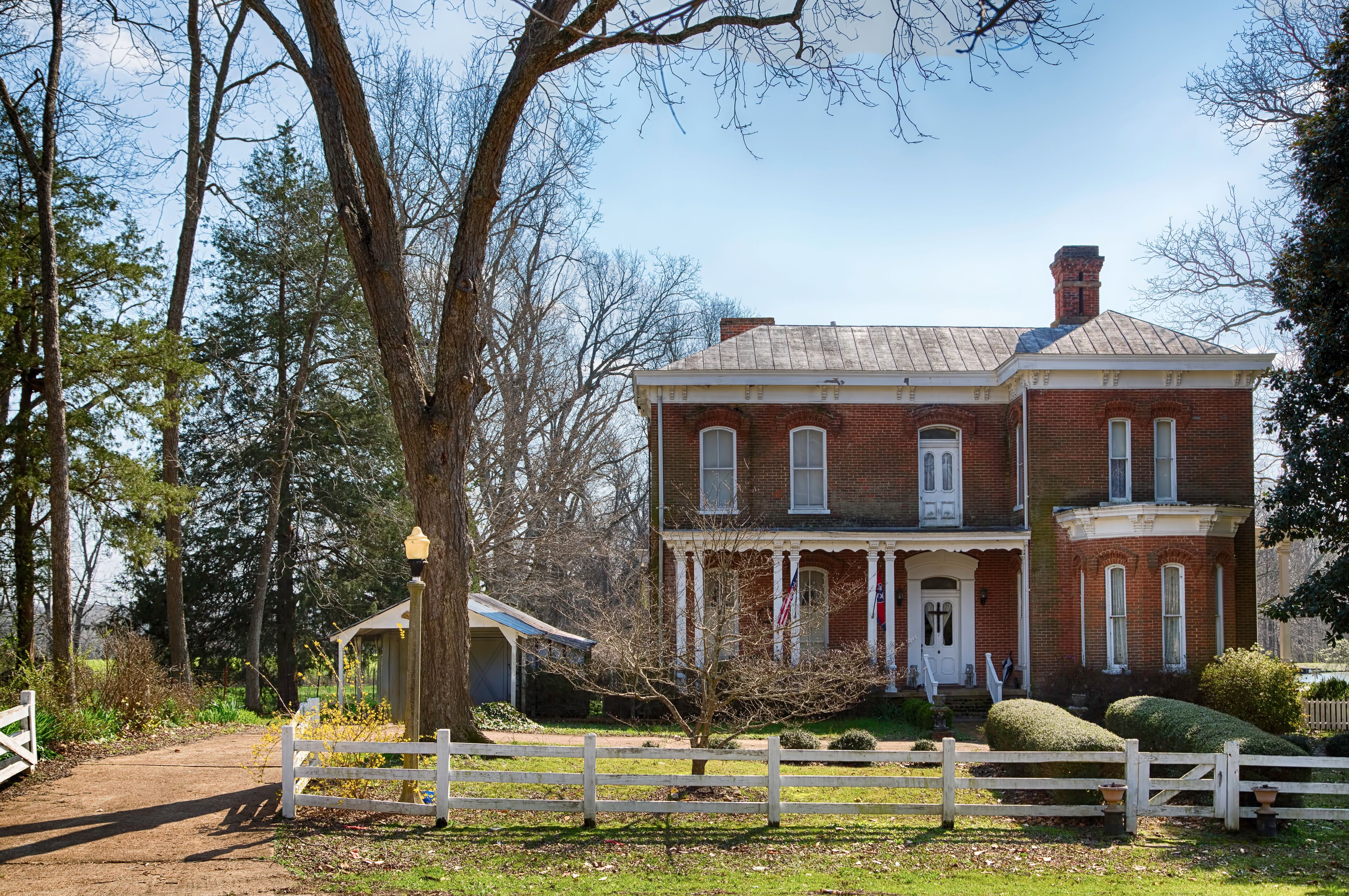 A red brick house with a white porch and a small shed.