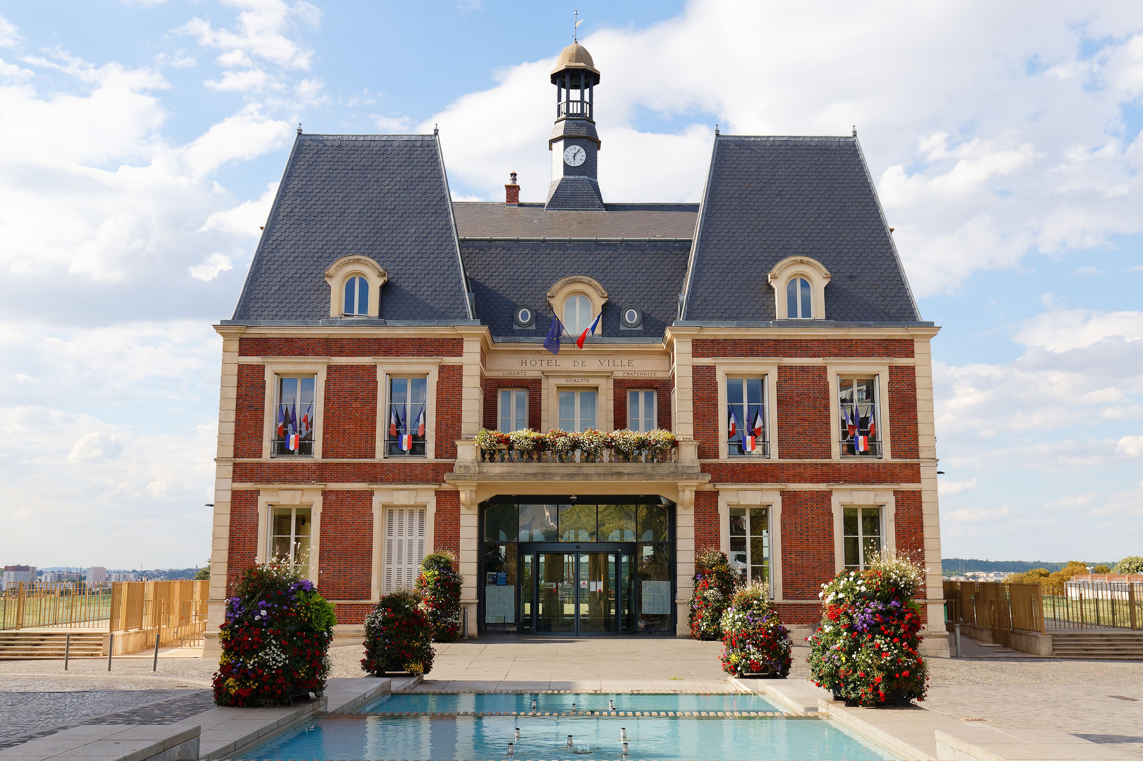A large brick building with a clock tower, a swimming pool, and flags.