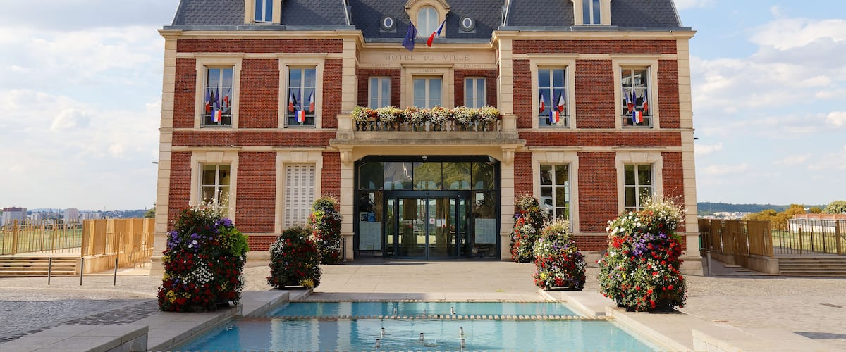 A large brick building with a clock tower, a swimming pool, and flags.