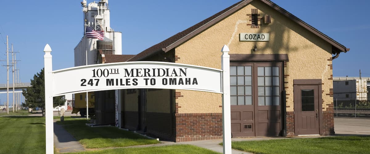 A grain elevator with a sign reading "100th Meridian 247 miles to Omaha" and a building labeled "COZAD".