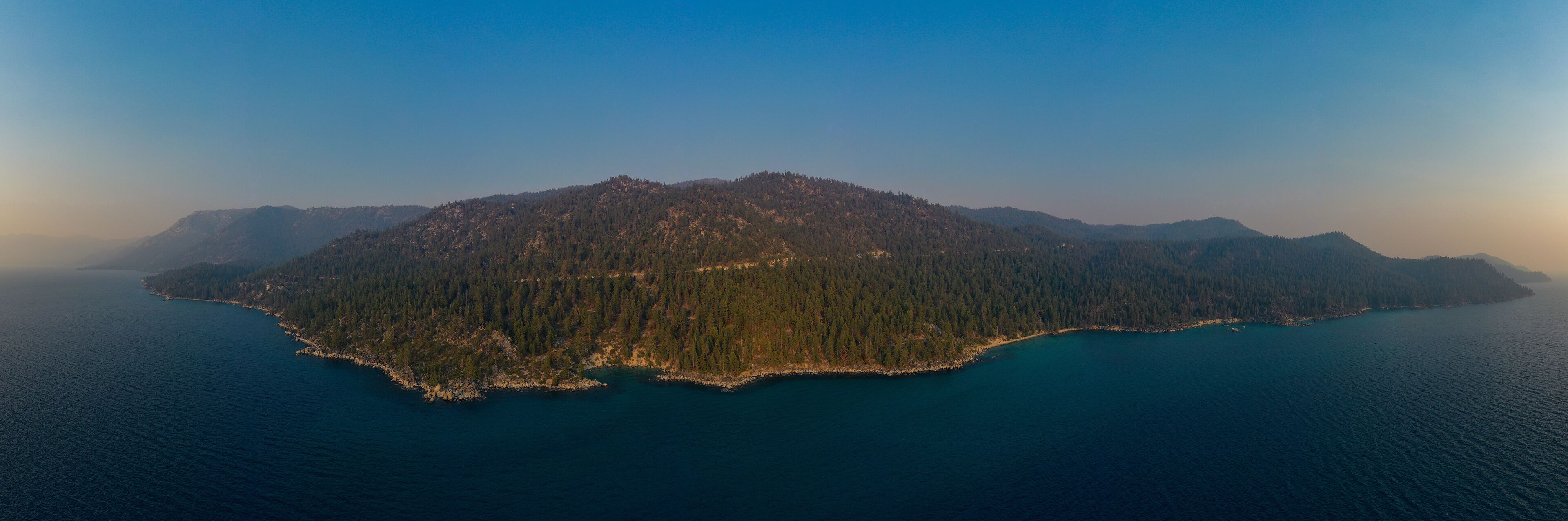 An aerial view of a forested island surrounded by deep blue water.