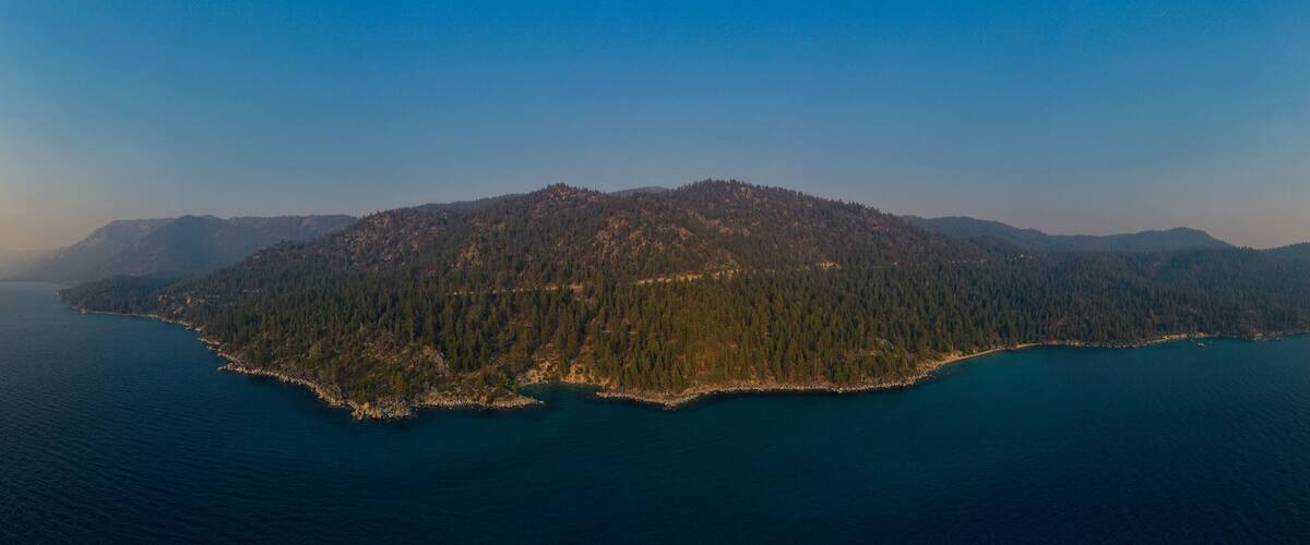 An aerial view of a forested island surrounded by deep blue water.